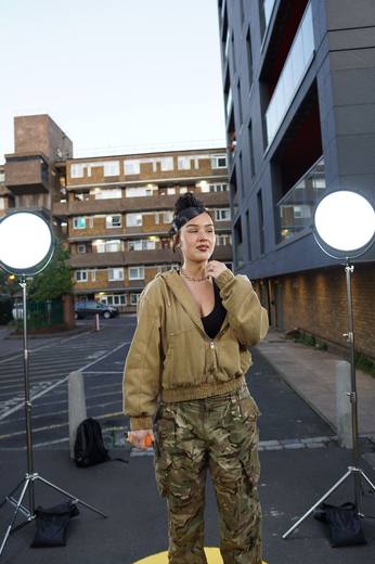 A singer in a khaki jacket and camo trousers performing between two ring lights in a London estate courtyard