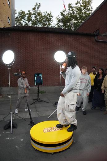 An artist in a white top performing on the booth while the crowd watches along the wall