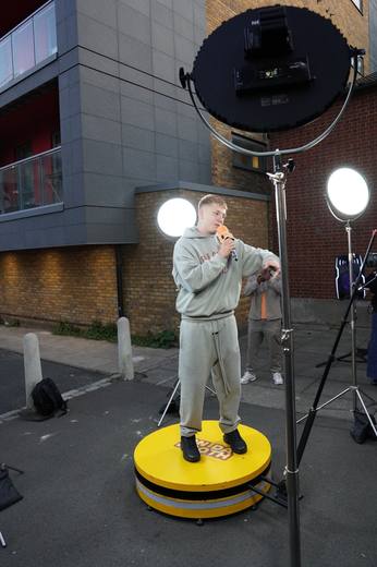 The artist in the grey tracksuit performing under a ring light, filmed from the side