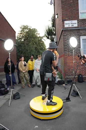 An artist in black performing on the booth outside a block of flats, with the crowd watching
