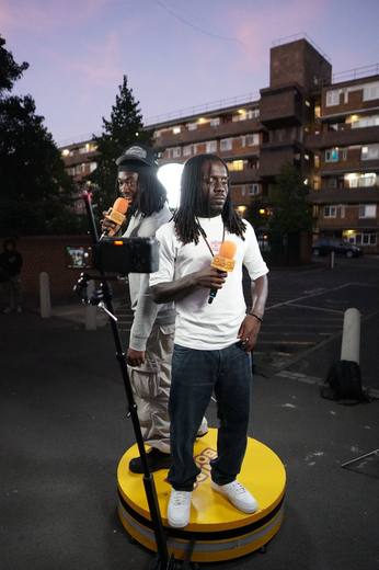 An artist in a white T-shirt performing at dusk, with the camera arm in the foreground